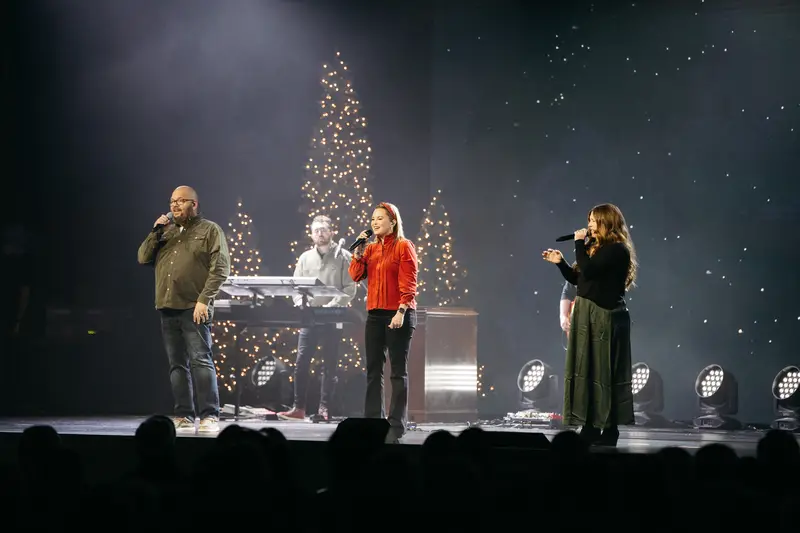 Singers on stage in front of lit Christmas trees and a starry backdrop